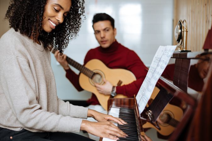 Woman playing piano near man playing guitar in studio