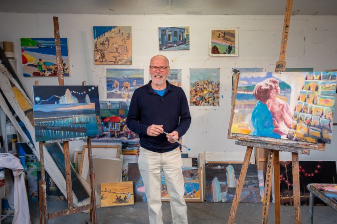 Happy older male surrounded by paintings in art studio