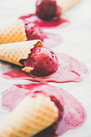 Cones of dark berry ice cream melting on marble slab, vertical composition, side view