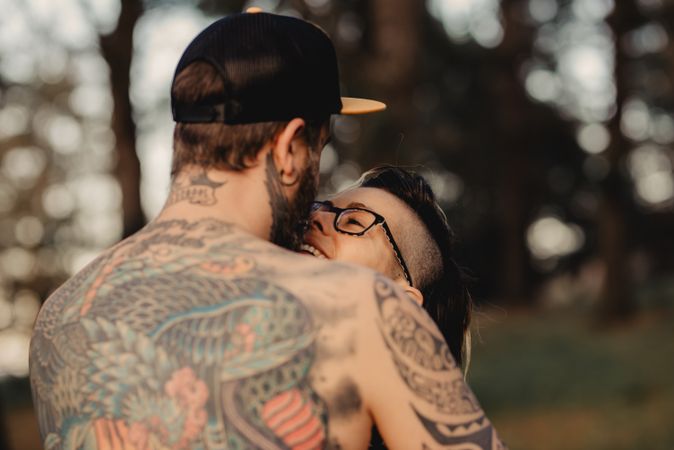 Happy couple hugging and kissing near tree in park