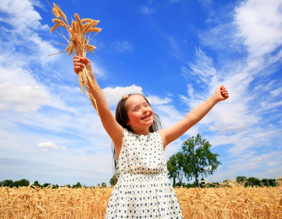 Joyful young girl with Down syndrome holding a chaff of wheat in a field