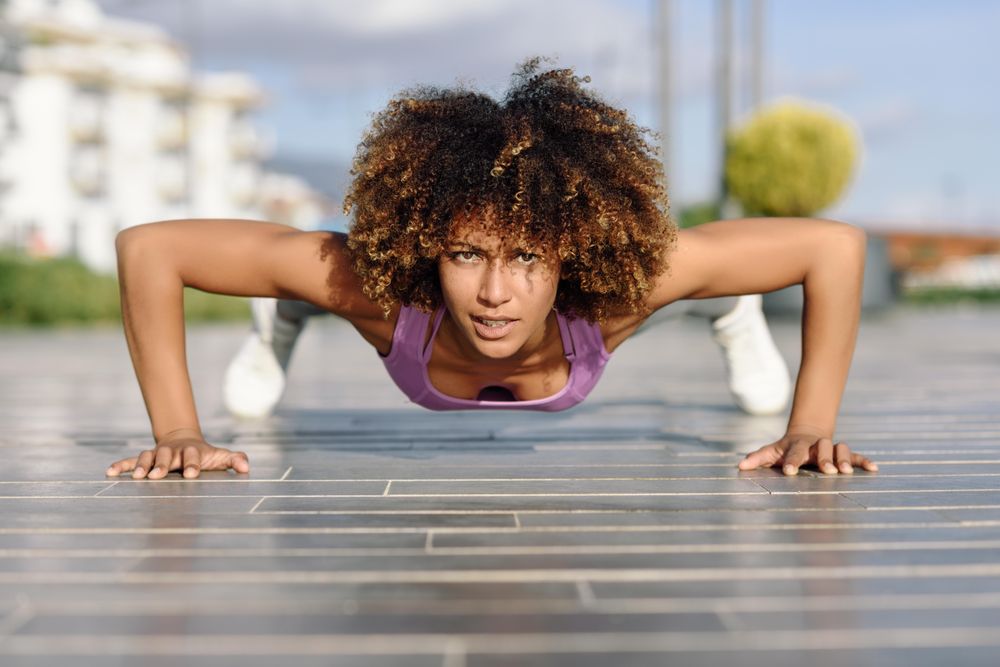 Fit female with afro hairstyle doing planks outside