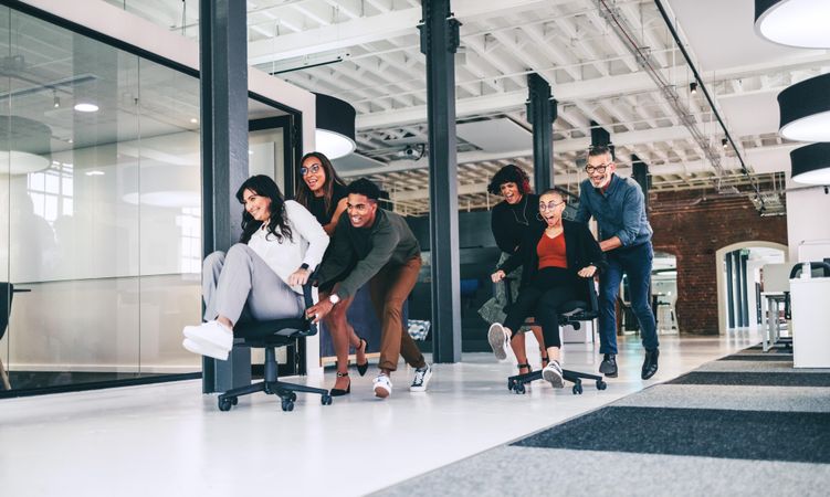 Team of businesspeople having fun together in an office in office chair race