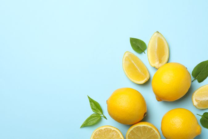 Fresh lemons with leaves on blue background, top view. Ripe fruit