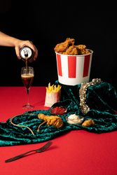 Woman pouring soda in wineglass beside collections of jewelry and fast food