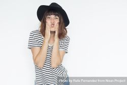 Female in striped shirt and felt hat holding mouth making funny face, copy space 0PlAa0
