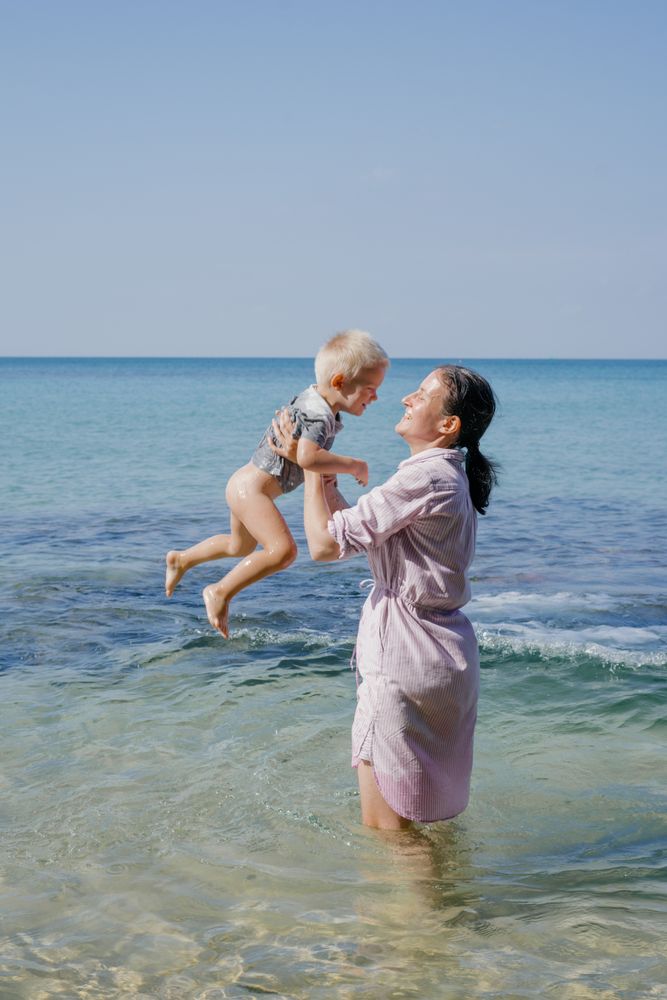 Woman and small kid having fun with water while relaxing on seacoast at resort