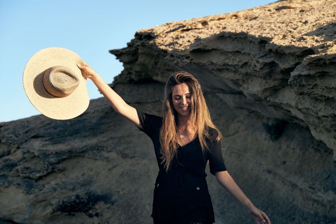 Cheerful woman holding hat in air