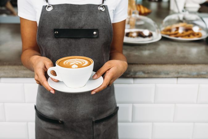 Barista in apron holding large cappuccino