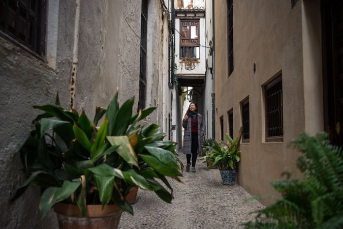 Female traveler in casual clothing at alley with quick pot of flowers