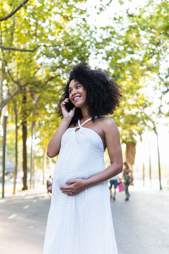 Smiling Black pregnant woman talking on smartphone