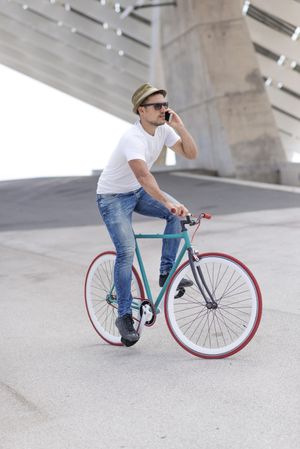 Male in hat having a relaxing bicycle ride outside using phone