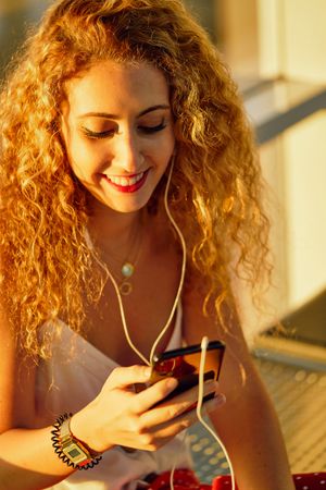 Smiling woman sitting on metal bench with earphones and smartphone
