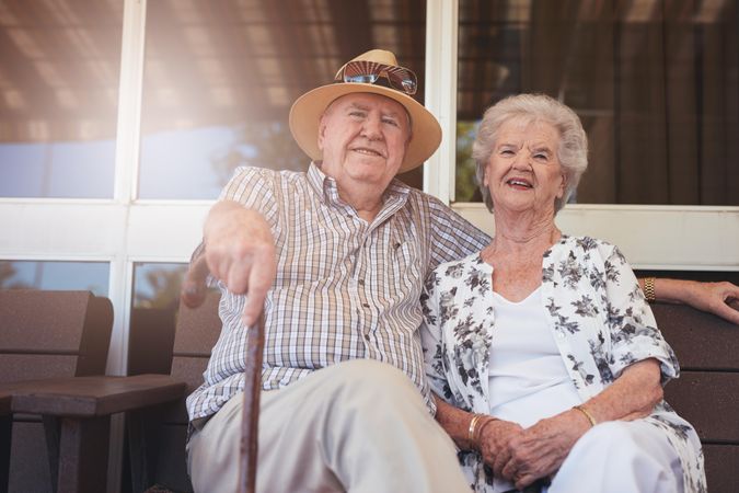 Portrait of loving older couple relaxing on a bench outside their house