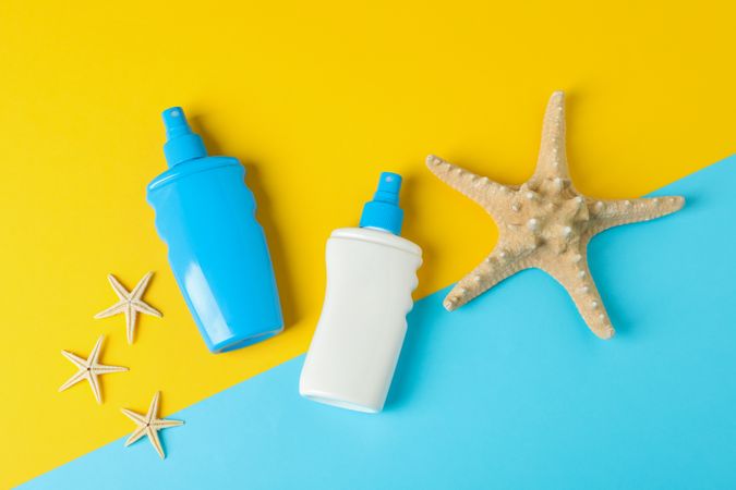 Flat lay composition with sunscreen sprays and starfishes on two tone background, space for text. Summer vacation backdrop