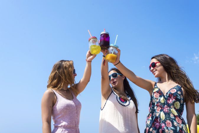 Group of smiling female friends toasting non alcoholic drinks on summer beach