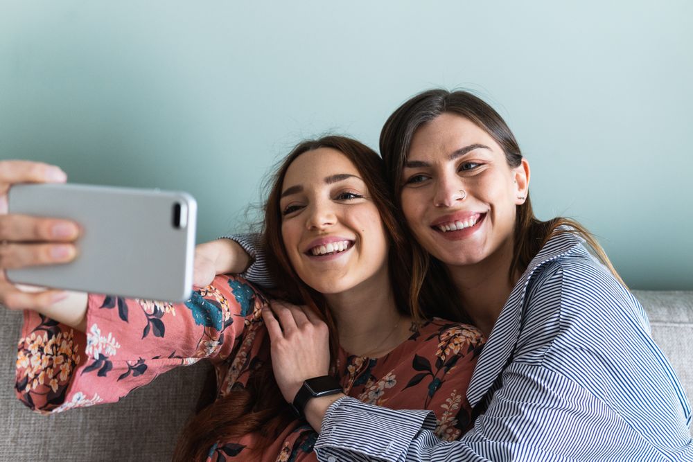 Smiling women hugging and taking selfie on smartphone
