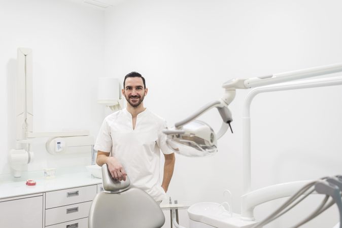 Portrait of a handsome dentist wearing a light uniform, standing in a clinic