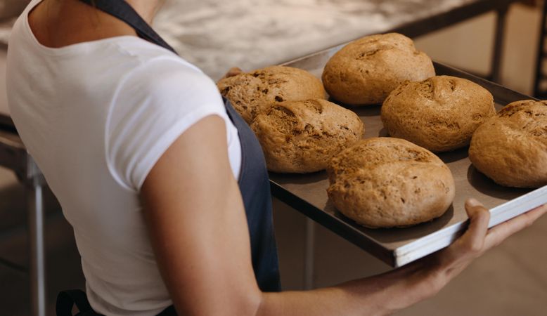 Close up of female baker holding a freshly baked bread on a baking tray