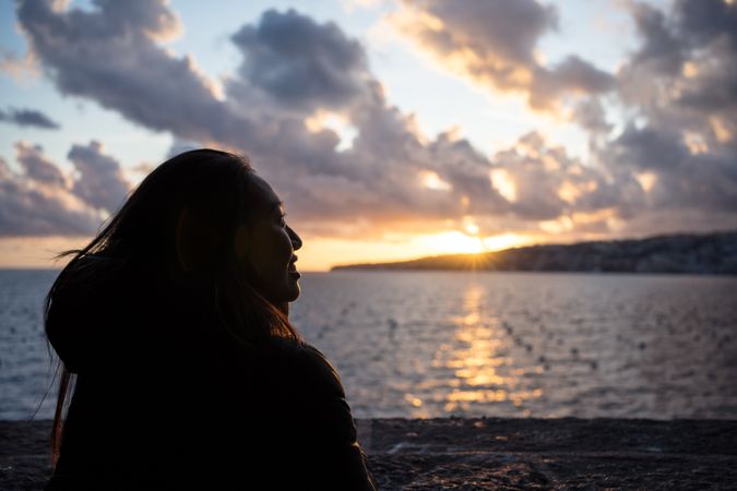 Joyful female on vacation in warm wear delighting in sunset on seashore