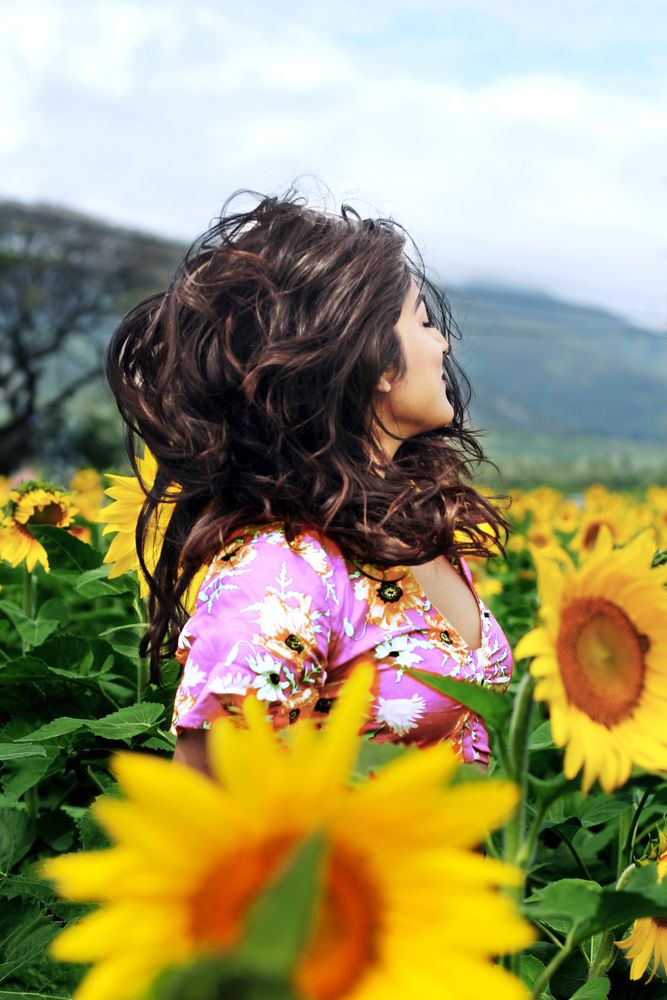 Woman in pink and yellow floral shirt standing on sunflower field