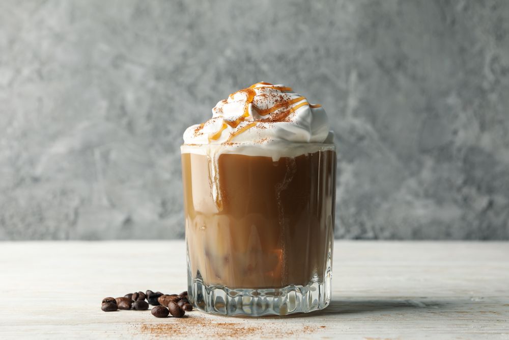 Glass of ice coffee with poured cream on wooden table