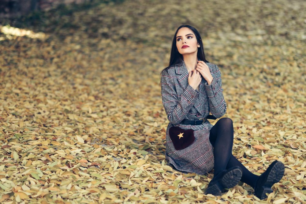 Content female sitting relaxing in park in fall time with colorful leaves on ground