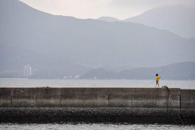 Fisherman standing on concrete fishing dock near mountains