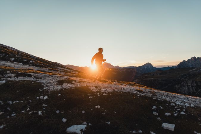 Man in red jacket walking on shrubland at sunset