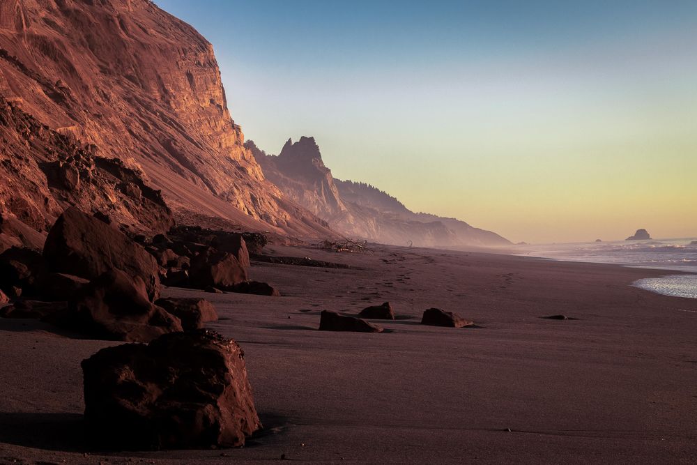 Rocky boulders on a sandy beach with cliffs and mist