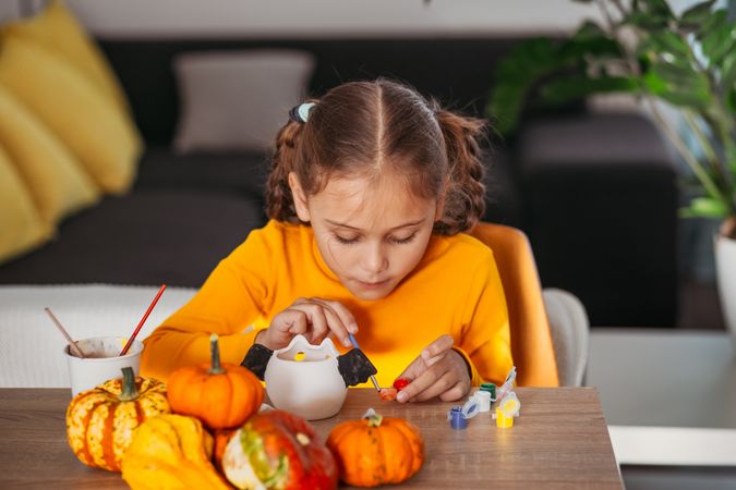A little girl paints a clay hand made pumpkin. Halloween party. Crafts for children.