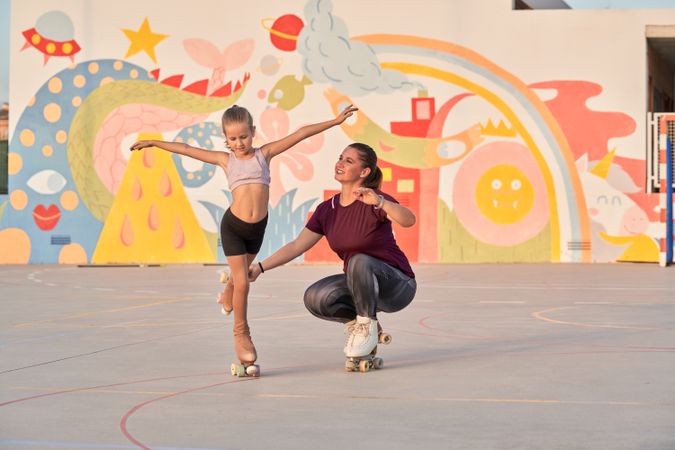 Woman helping girl to do exercise on roller skates