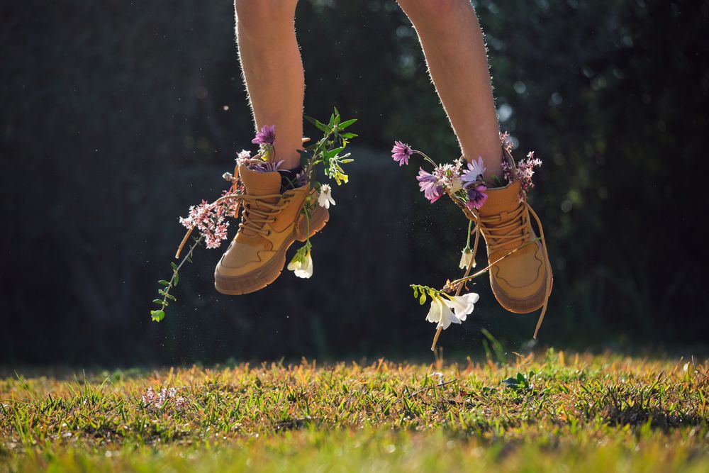 Crop person in boots with flowers jumping in nature