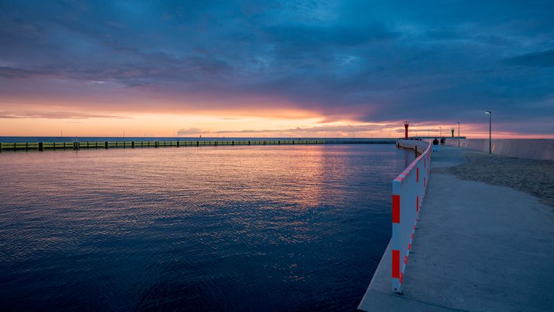 Tranquil sea, twilight hues, guiding lighthouse by the shore.