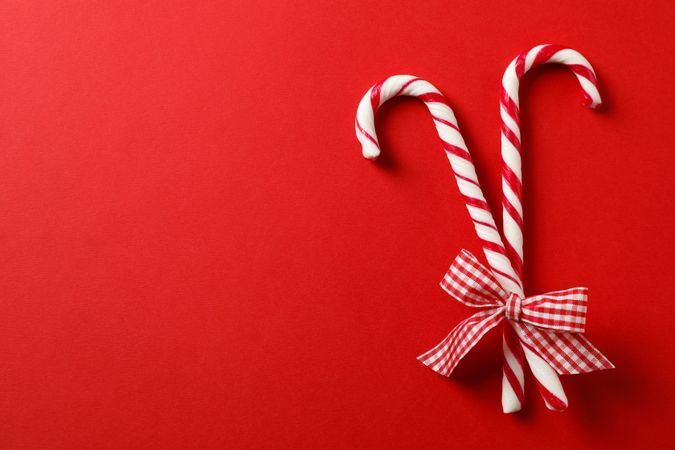 Sweet candy canes with bow on red background, space for text