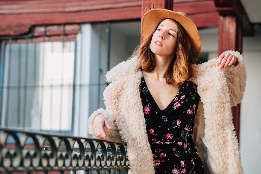 Smiling woman in warm wear standing near building and fence