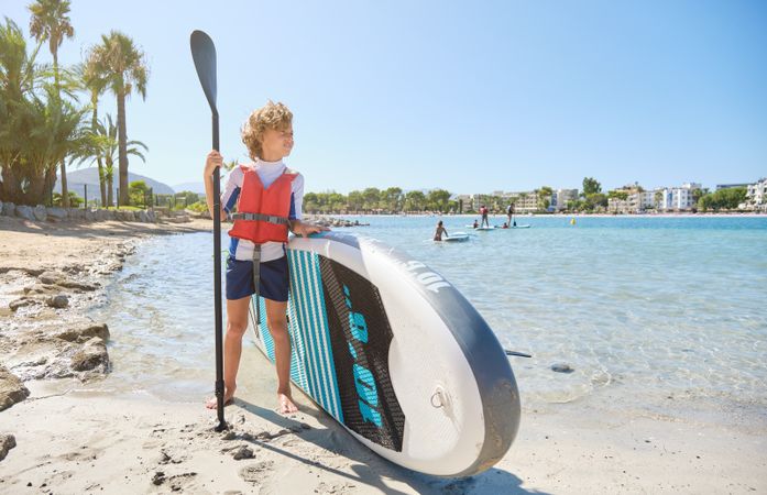 Boy with paddleboard on sandy beach