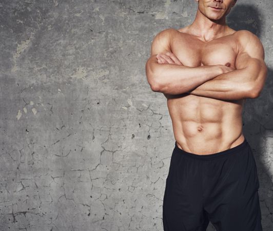 Portrait of muscular man’s torso against concrete wall