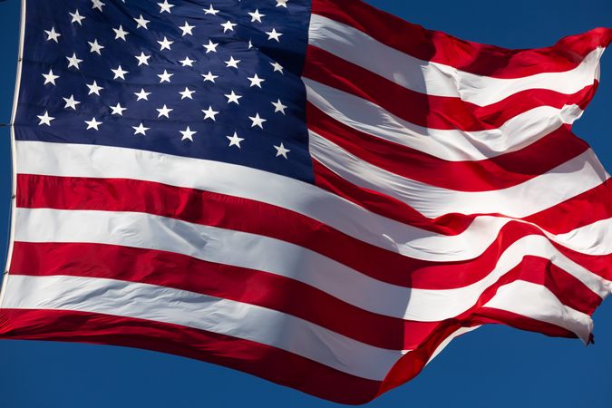 American Flag Waving In The Wind Against Deep Blue Sky.