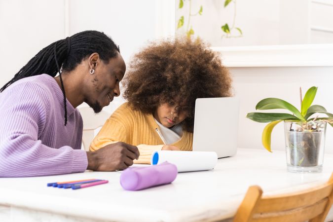 Black father helping daughter with homework on laptop