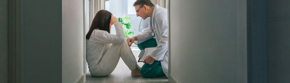 Doctor reassuring with empathy a patient sitting on the floor of a mental health center