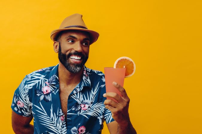 Happy male about to enjoy a cocktail while wearing colorful shirt with yellow background