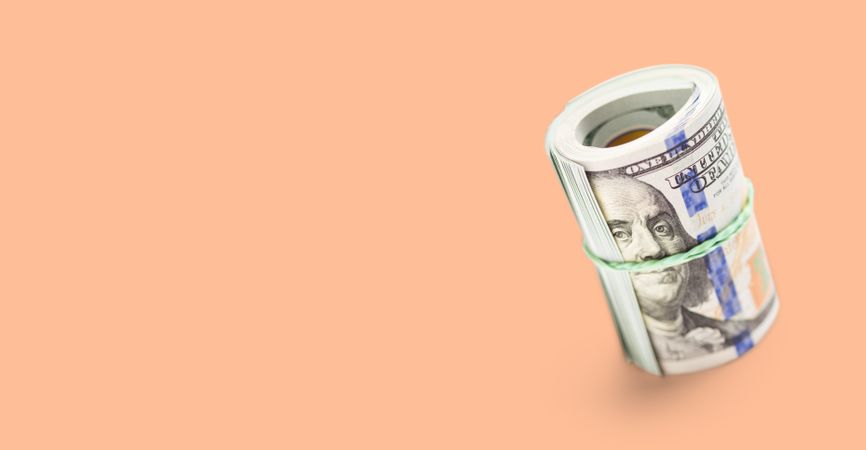 Roll Of One Hundred Dollar Bills Secured with a Rubber Band on a Peach Fuzz Background.
