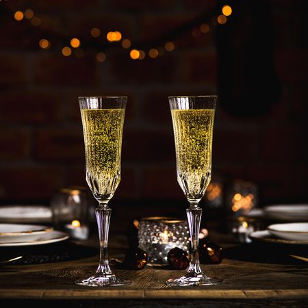 Two crystal flutes full of champagne on wooden table, square crop