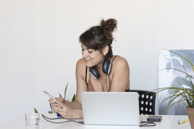 Female smiling at something on phone in front of laptop in home office
