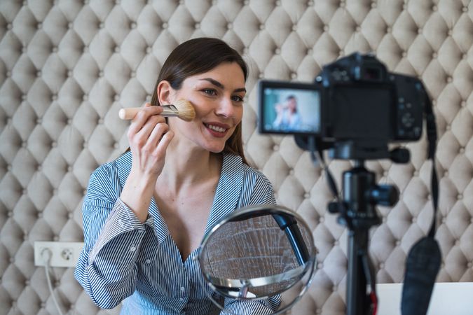 Happy woman applying powder and recording video on camera