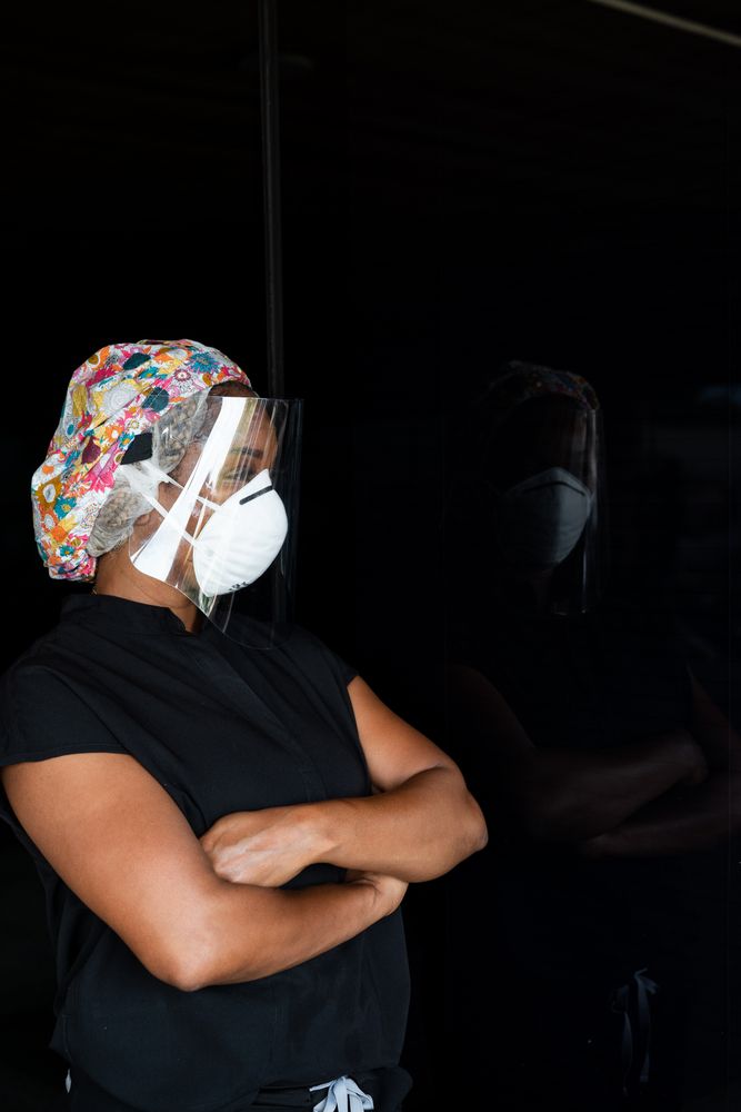Portrait of woman nurse with arms crossed wearing face shield looking into dark window