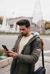 Young male in warm jacket using smartphone