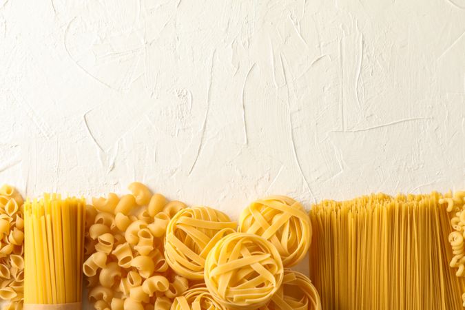 Different pasta on light background, space for text. Dry uncooked whole pasta