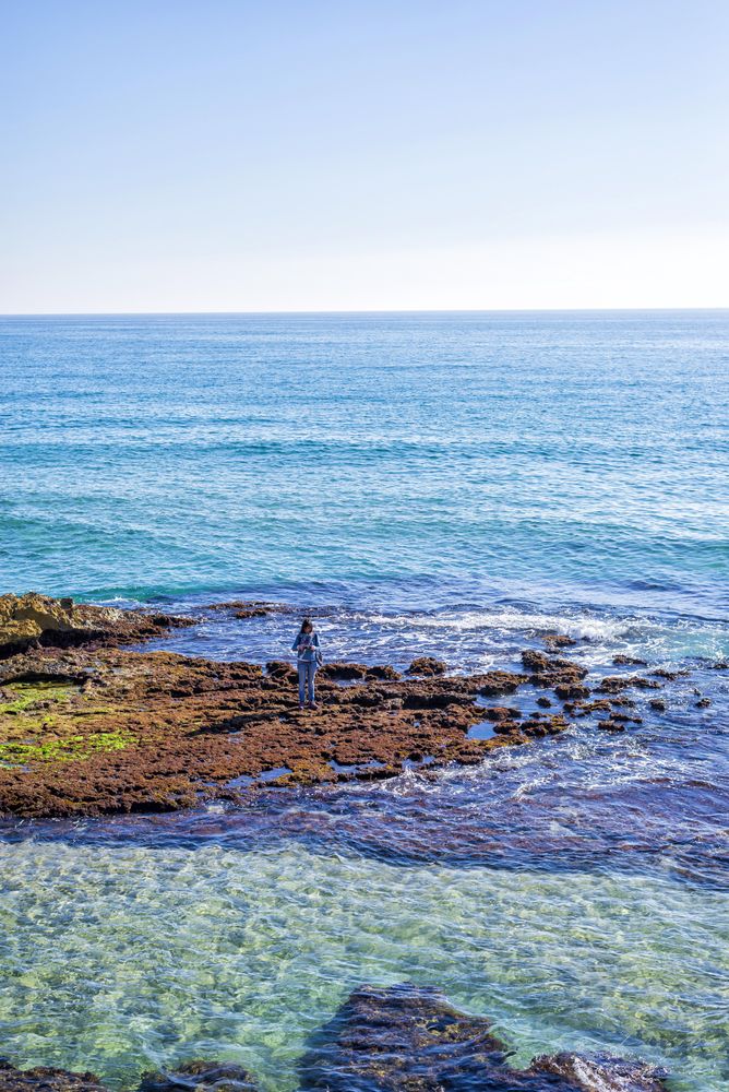 Female dressed in blue standing on coastal rocks near water